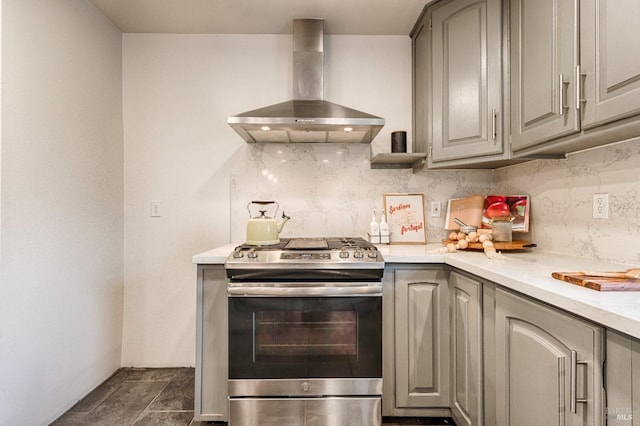 kitchen with gray cabinets, wall chimney range hood, backsplash, and gas range