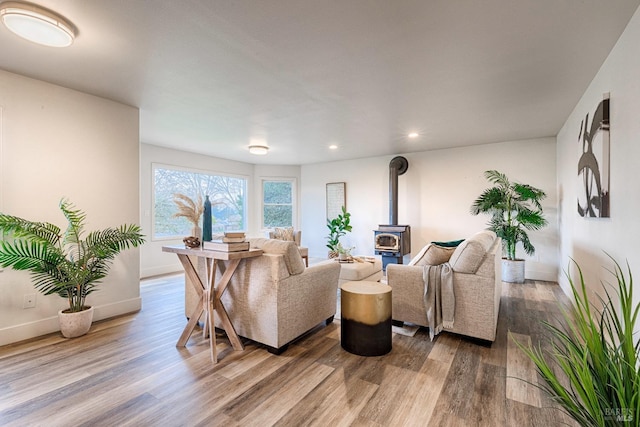 living room with recessed lighting, a wood stove, baseboards, and wood finished floors