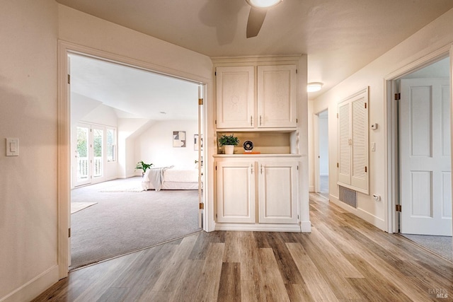 hall with light carpet, baseboards, visible vents, and light wood-style floors