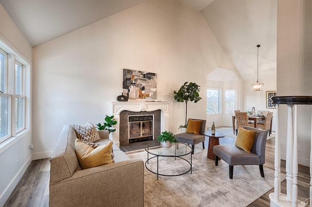 living room featuring high vaulted ceiling, a fireplace, wood finished floors, baseboards, and an inviting chandelier