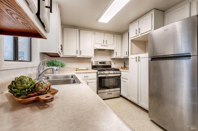 kitchen with light countertops, appliances with stainless steel finishes, white cabinetry, a sink, and under cabinet range hood