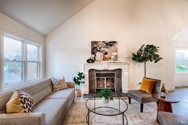 living area featuring high vaulted ceiling, a tile fireplace, baseboards, and wood finished floors