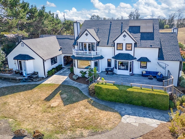 view of front of house with roof with shingles, a chimney, an outdoor hangout area, a balcony, and a front lawn