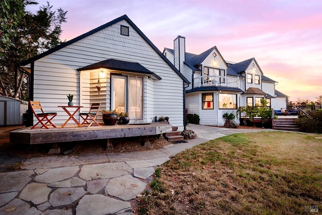 rear view of house with a lawn, a balcony, an outbuilding, a storage unit, and a deck