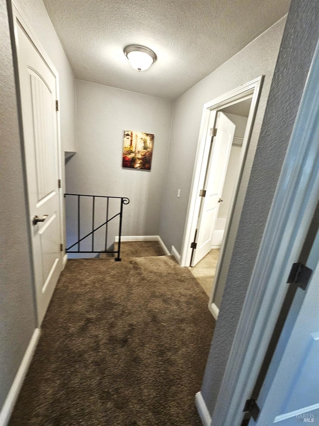 corridor with carpet, a textured ceiling, and baseboards