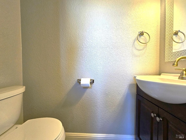 bathroom featuring a textured wall, vanity, toilet, and baseboards