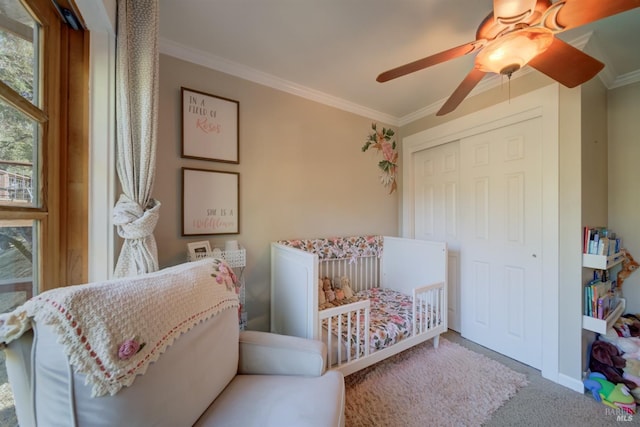 carpeted bedroom featuring ornamental molding, a nursery area, ceiling fan, and a closet