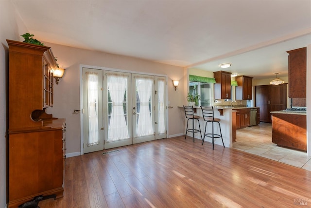 kitchen with light wood-type flooring, kitchen peninsula, a breakfast bar, stainless steel dishwasher, and pendant lighting