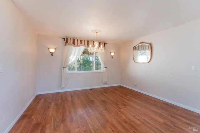 empty room with hardwood / wood-style flooring and an inviting chandelier