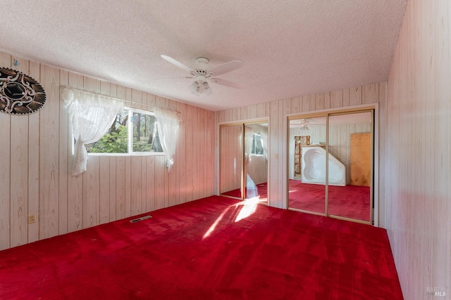 unfurnished bedroom with ceiling fan, multiple closets, carpet floors, and a textured ceiling