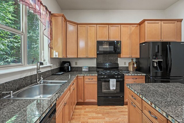 kitchen featuring dark stone counters, a sink, light wood-style flooring, and black appliances