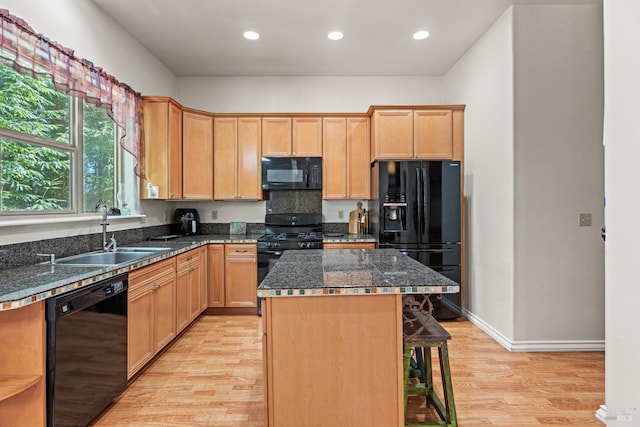 kitchen with light hardwood / wood-style flooring, sink, black appliances, a kitchen breakfast bar, and a kitchen island