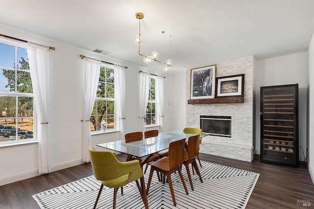 dining area featuring dark hardwood / wood-style floors, a stone fireplace, wine cooler, and a chandelier