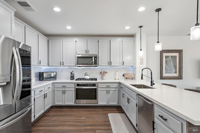 kitchen with dark wood-type flooring, stainless steel appliances, sink, hanging light fixtures, and kitchen peninsula