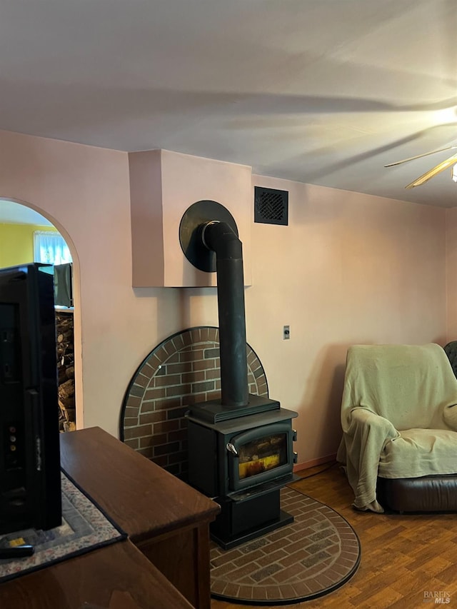 interior space with ceiling fan, a wood stove, and hardwood / wood-style flooring