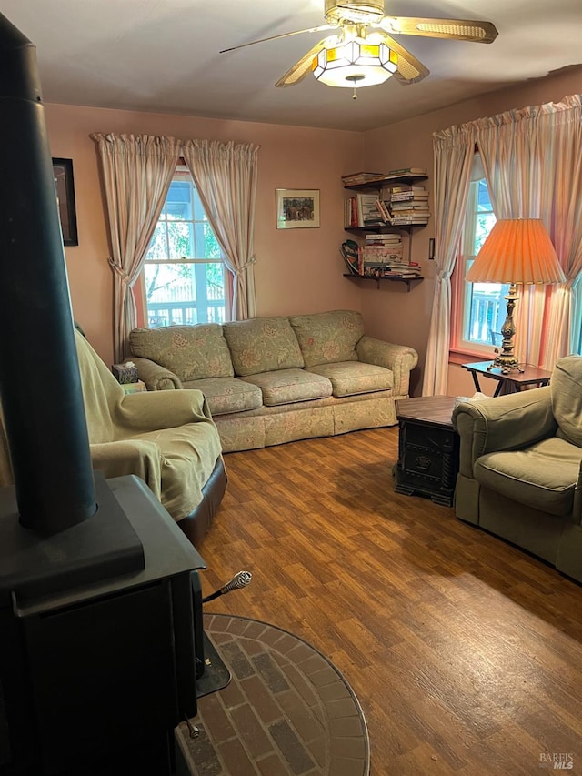 living room with a wood stove, wood-type flooring, and ceiling fan