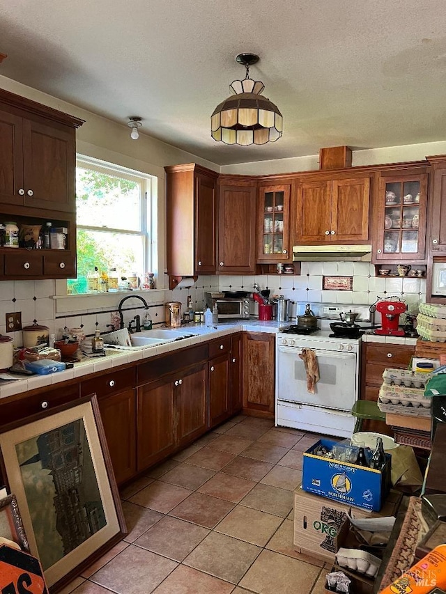 kitchen featuring hanging light fixtures, light tile patterned flooring, tile countertops, white range with gas cooktop, and sink