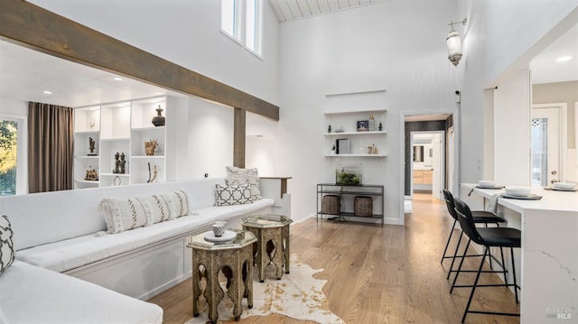 living room featuring beam ceiling, light hardwood / wood-style flooring, and a towering ceiling