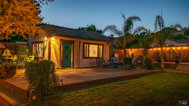 back house at dusk with a deck and a lawn