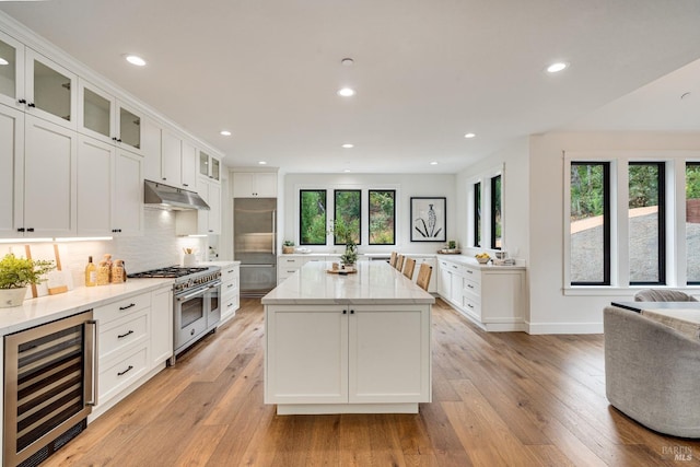 kitchen featuring plenty of natural light, high end appliances, wine cooler, and light hardwood / wood-style floors