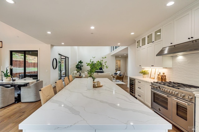 kitchen with double oven range, light stone counters, white cabinets, and light hardwood / wood-style floors