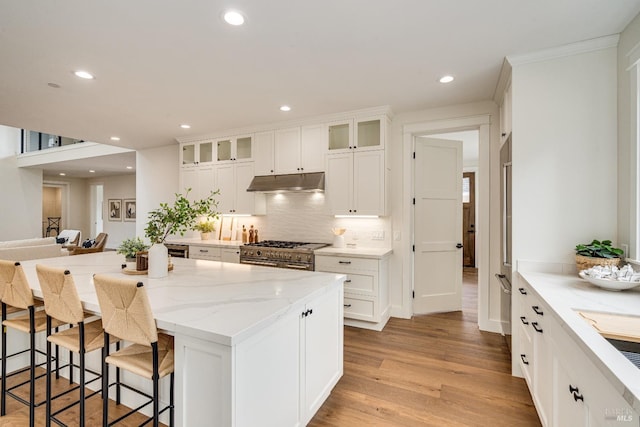 kitchen featuring white cabinets, a kitchen breakfast bar, high end stove, and light hardwood / wood-style flooring