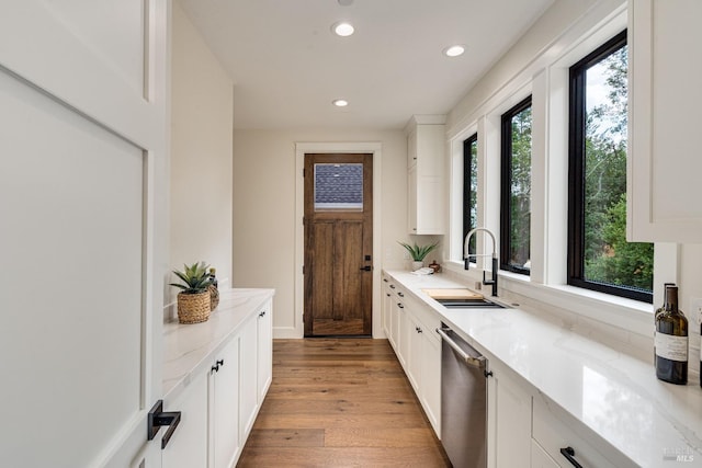 kitchen with dishwasher, sink, light stone counters, light wood-type flooring, and white cabinets