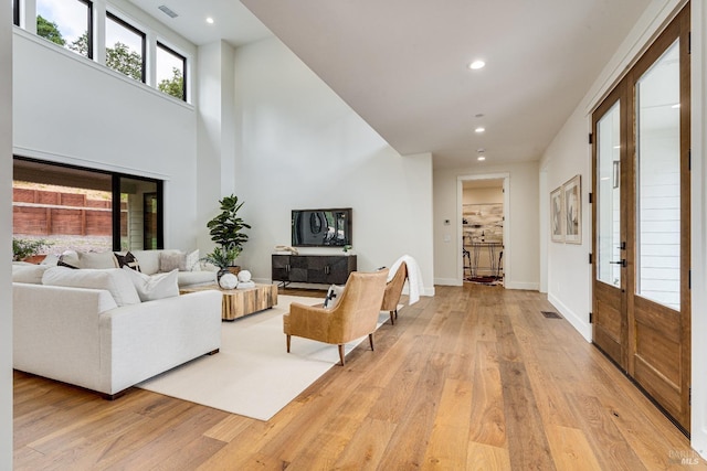 living room with a towering ceiling, french doors, and light hardwood / wood-style floors