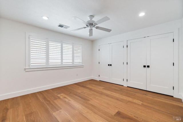 unfurnished bedroom featuring multiple closets, visible vents, light wood-style flooring, and baseboards