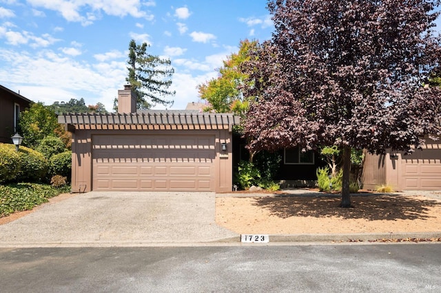 view of property hidden behind natural elements featuring concrete driveway, a chimney, and a tile roof