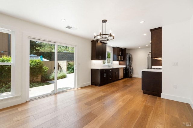 kitchen featuring visible vents, light countertops, light wood-type flooring, stacked washer and clothes dryer, and pendant lighting