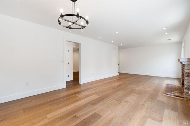 unfurnished living room with light wood-style floors, a fireplace, baseboards, and a chandelier