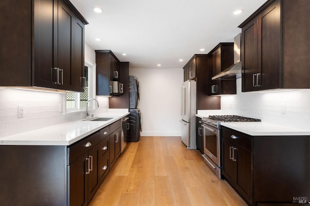 kitchen featuring premium appliances, light countertops, light wood-style floors, a sink, and wall chimney exhaust hood