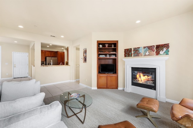 living area featuring visible vents, built in shelves, baseboards, recessed lighting, and a glass covered fireplace