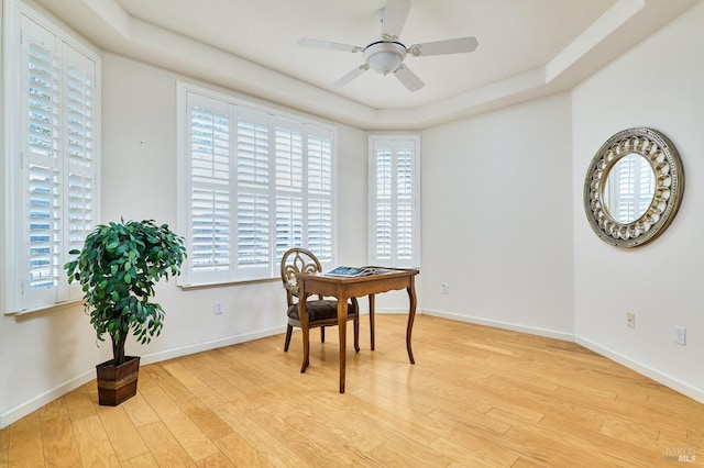 dining room featuring light wood-type flooring, a tray ceiling, and ceiling fan