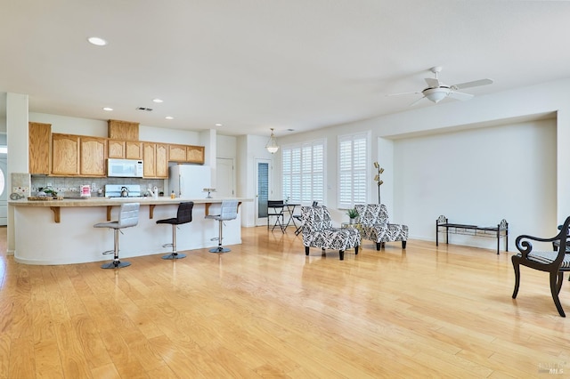 interior space featuring light wood-type flooring, white appliances, ceiling fan, tasteful backsplash, and a breakfast bar