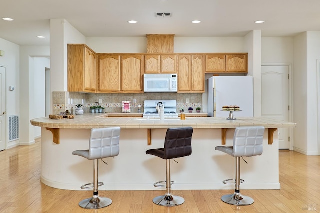 kitchen with white appliances, light hardwood / wood-style flooring, a kitchen bar, and tasteful backsplash