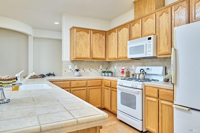 kitchen featuring white appliances, backsplash, kitchen peninsula, sink, and light hardwood / wood-style floors