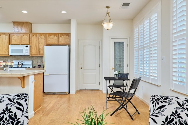 kitchen featuring light wood-type flooring, pendant lighting, white appliances, backsplash, and a breakfast bar