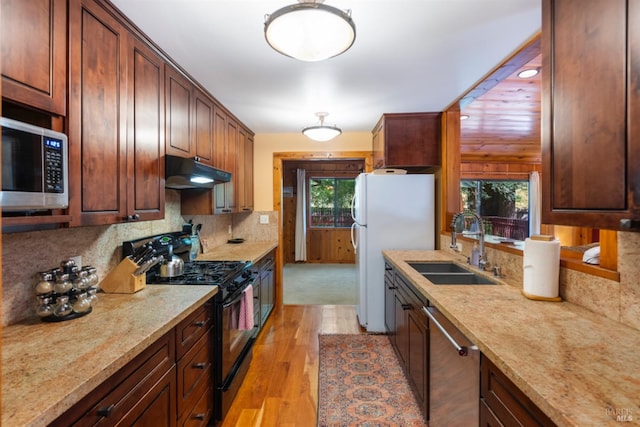 kitchen with appliances with stainless steel finishes, sink, decorative backsplash, light stone counters, and light wood-type flooring