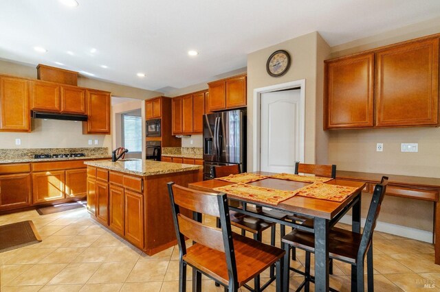 kitchen with black appliances, a kitchen island, light stone counters, and light tile patterned flooring