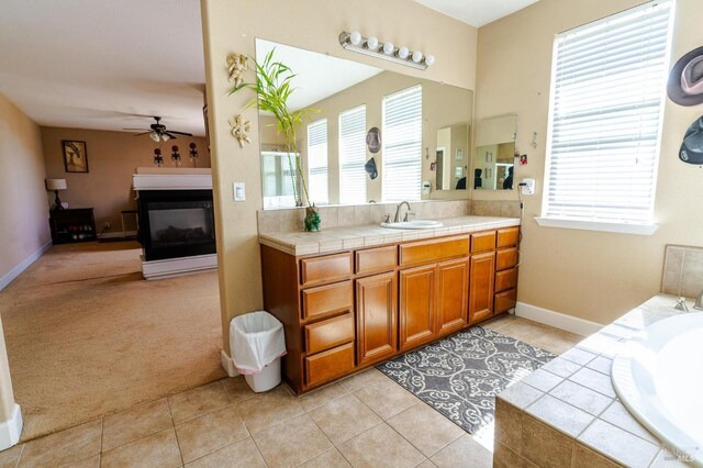 bathroom featuring ceiling fan, a multi sided fireplace, tile patterned floors, tiled tub, and vanity