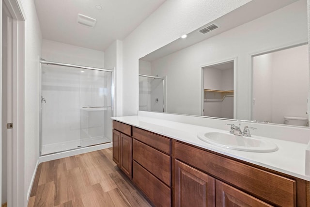 bathroom featuring visible vents, toilet, wood finished floors, vanity, and a shower stall