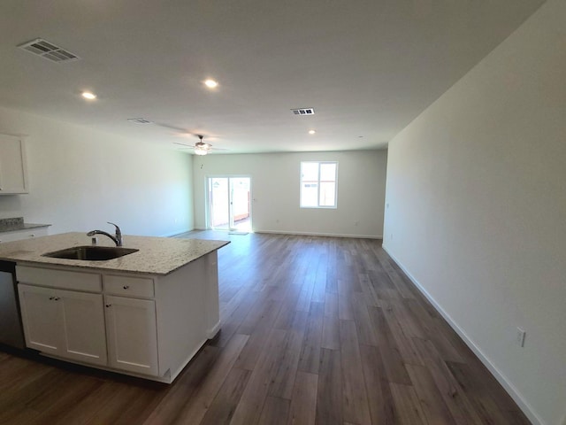 kitchen with light stone counters, dark wood-type flooring, sink, white cabinets, and an island with sink