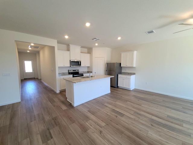 kitchen with sink, white cabinetry, stainless steel appliances, light stone counters, and a center island with sink