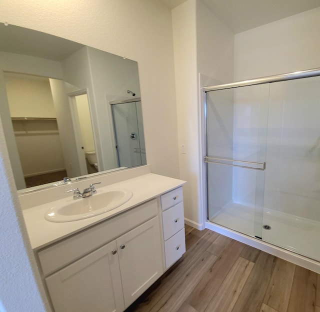 bathroom featuring toilet, wood finished floors, a walk in closet, vanity, and a shower stall