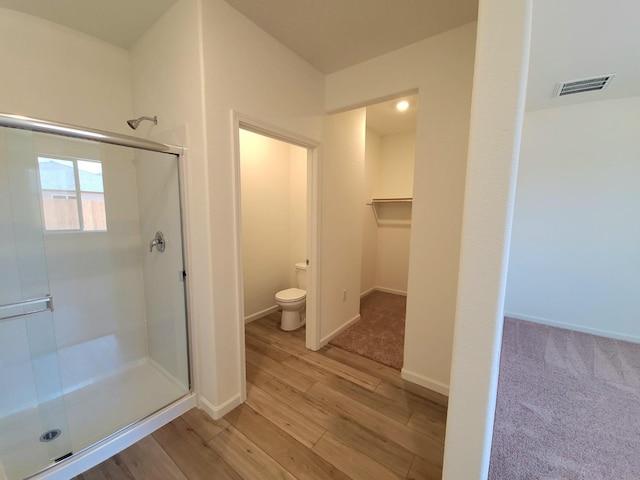 bathroom with a walk in closet, visible vents, toilet, a stall shower, and wood finished floors