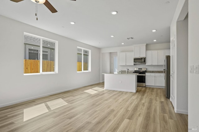 kitchen featuring light wood-type flooring, a kitchen island with sink, stainless steel appliances, ceiling fan, and white cabinets