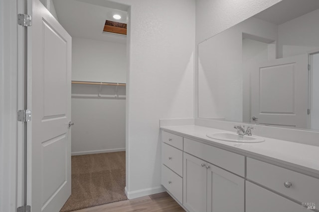 bathroom with wood finished floors, a walk in closet, vanity, and baseboards