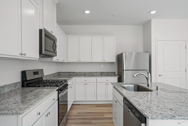 kitchen with a kitchen island with sink, stainless steel appliances, sink, white cabinetry, and light wood-type flooring